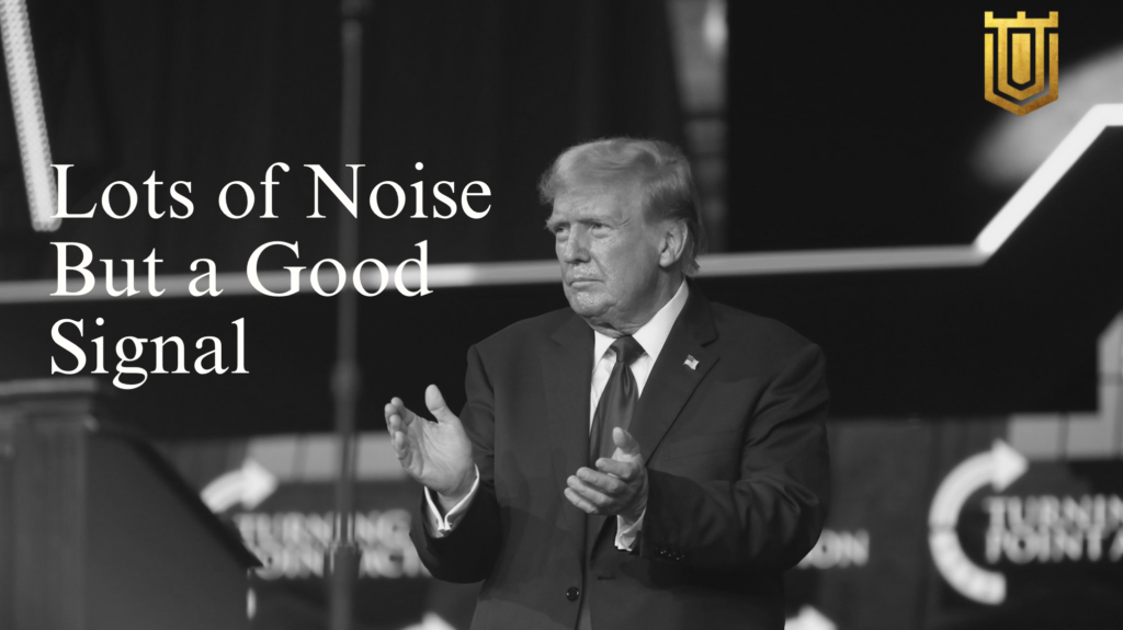 Black-and-white image of Donald Trump in a suit, holding a signed document at a wooden desk with phones and an American flag. Background features a large "Trump Gold Cap" poster with eagle motifs. Overlay text: "H1-B Changes" and gold shield emblem. Nicholas Mugalli from World Trade Securities offers analysis on immigration policy shifts and economic innovation.